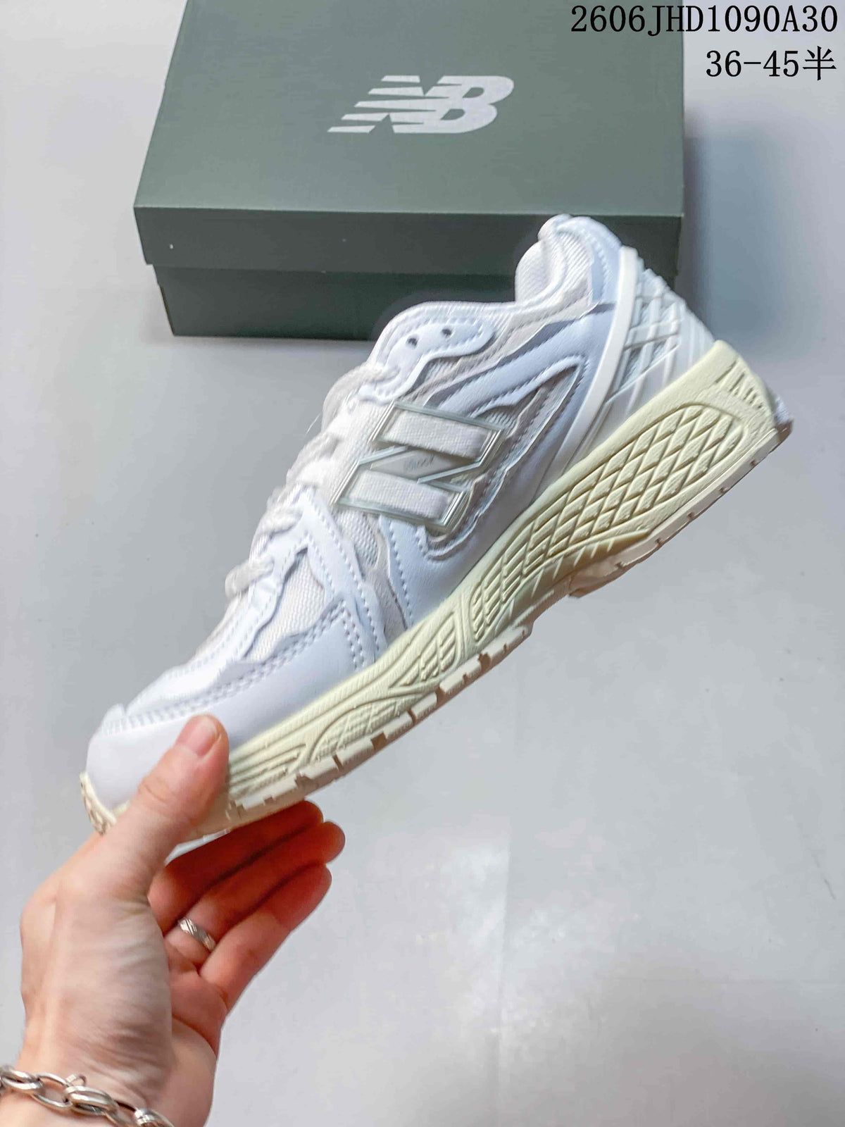 Side view of a white and silver-toned New Balance M1906R sneaker showing layered overlays and a cream-colored sole.