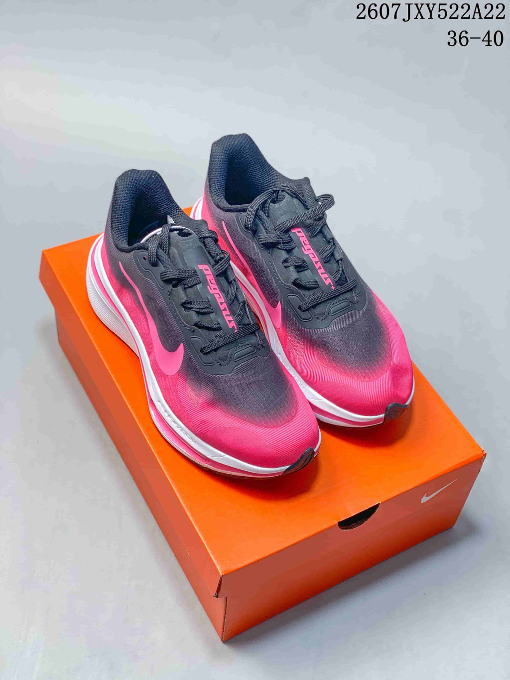 Pair of black and vivid pink Nike low-top sneakers displayed on an orange shoebox.