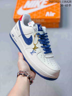 Angled side view showing the white and blue sneaker, decorative side markings, hanging charm, and red heel accent.