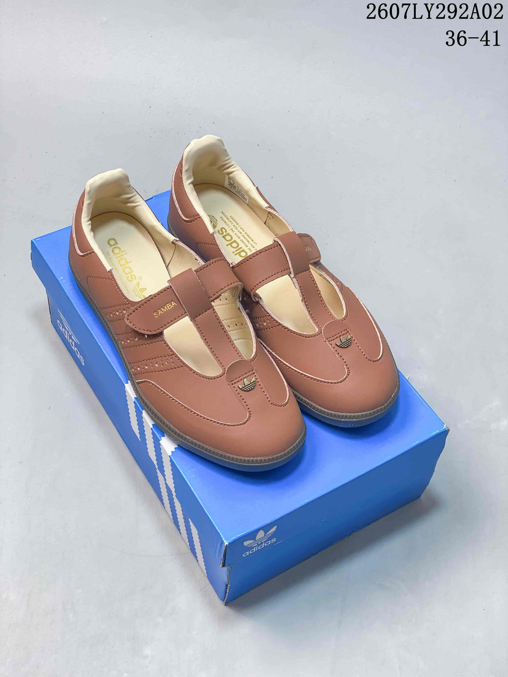 Pair of brown adidas Samba Jane-style Mary Jane sneakers displayed on a blue adidas shoebox, with the style code and size range visible above.