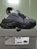 Balenciaga Triple S sneaker in gray and black shown on its box, with the box label visible below.