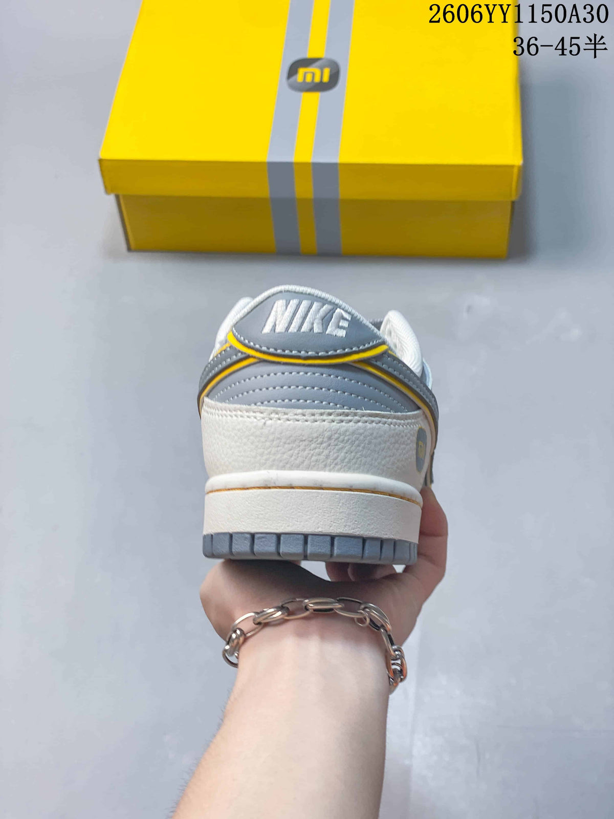 Rear view of a grey and white Nike SB Dunk Low sneaker with yellow trim
