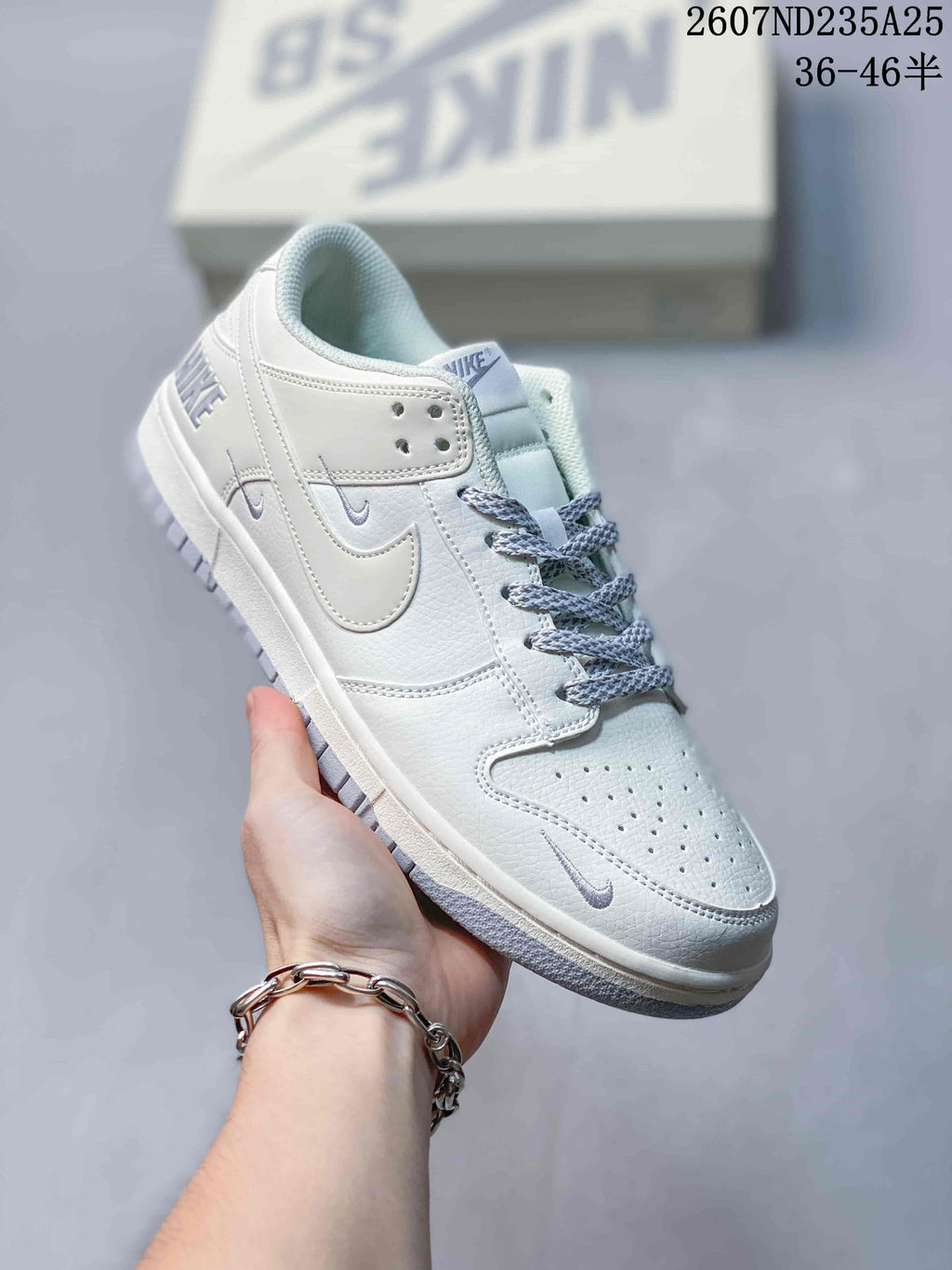 Handheld close-up of a white low-top sneaker with perforated toe, white Swoosh-style details and grey patterned laces.