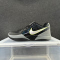 Side view of a black and gray Nike basketball sneaker with a light Swoosh outlined in yellow-green and a layered sole.