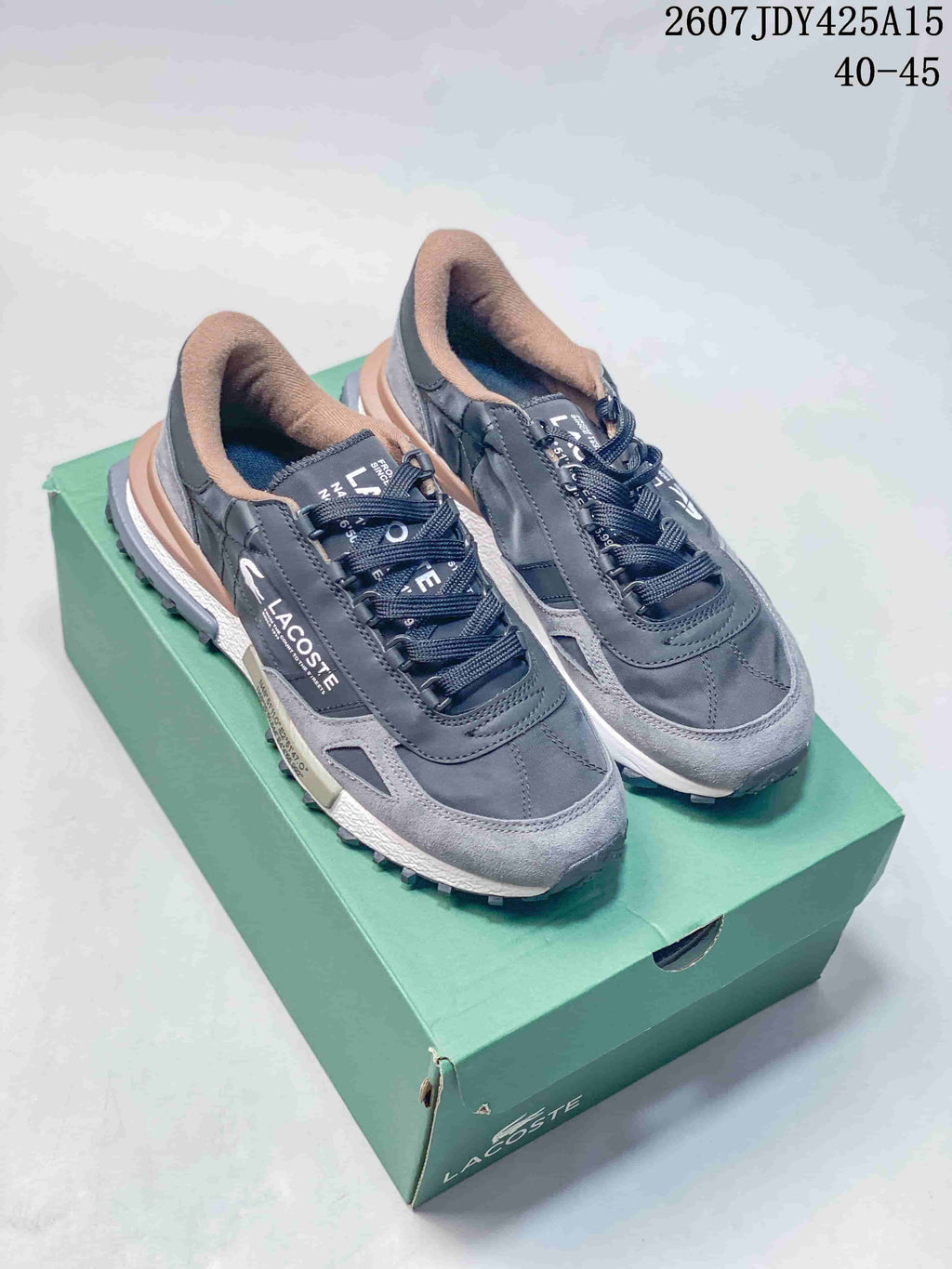 Pair of gray Lacoste lace-up sneakers displayed on a green shoebox, showing the layered upper and padded tan collars.