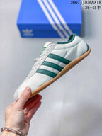 Side view showing the white upper, green three-stripe detailing, lace-up front and gum-colored sole.