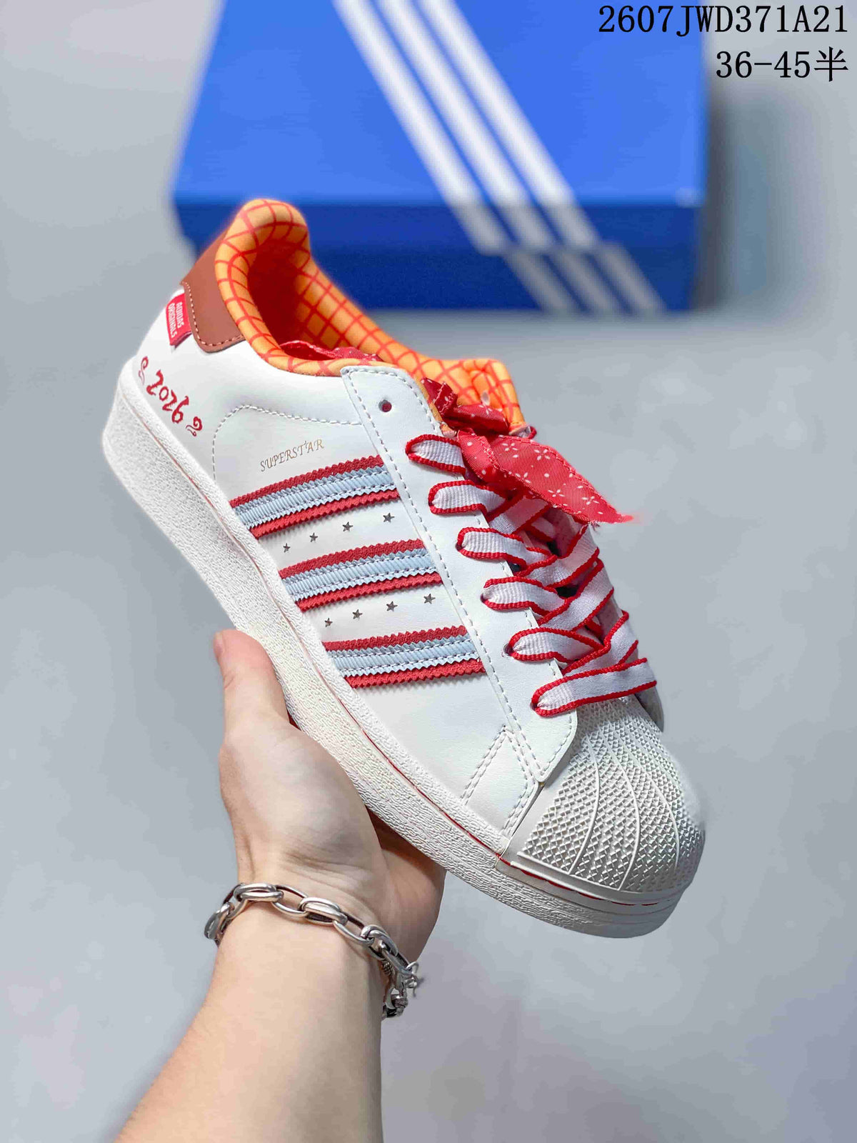 Angled side view showing the shell toe, white upper, striped side panel, red accents, and Superstar branding.