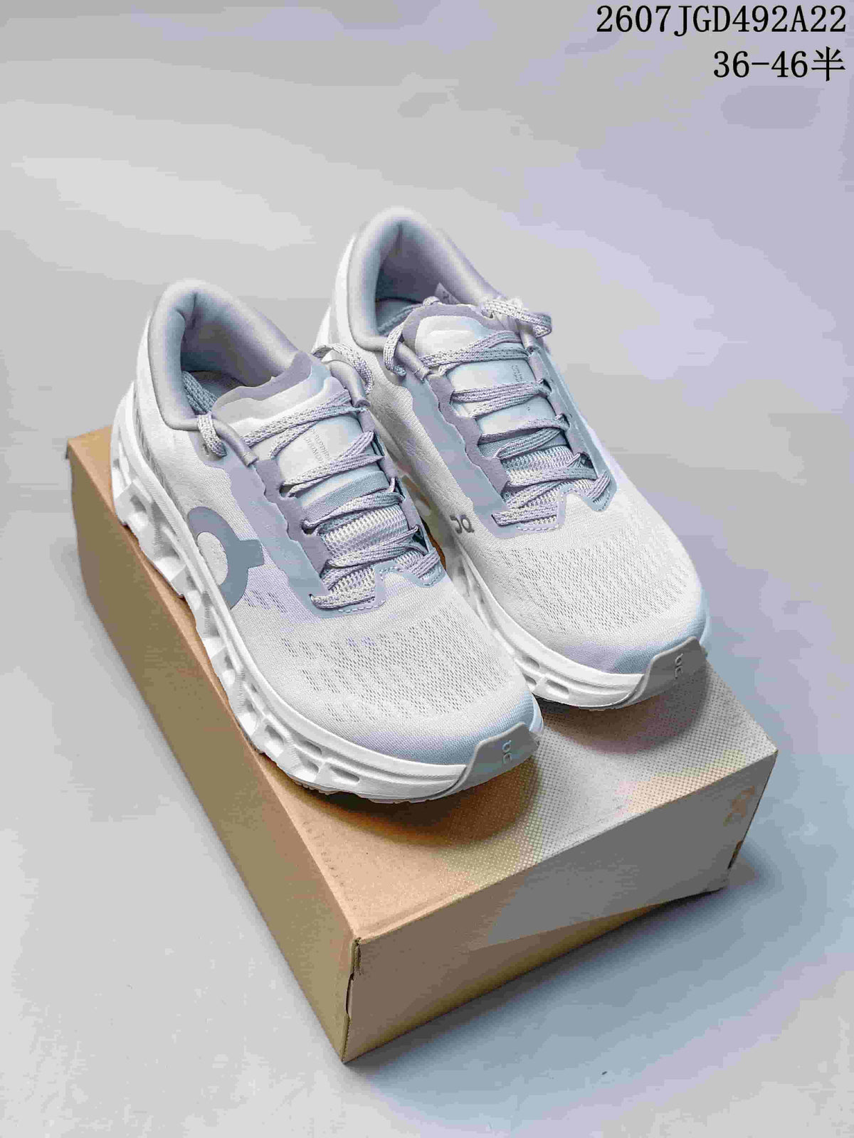 Pair of light gray and white On running shoes displayed on a tan shoebox.