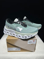 Pair of pale green Cloudmonster 2 shoes displayed on a box with a size label.
