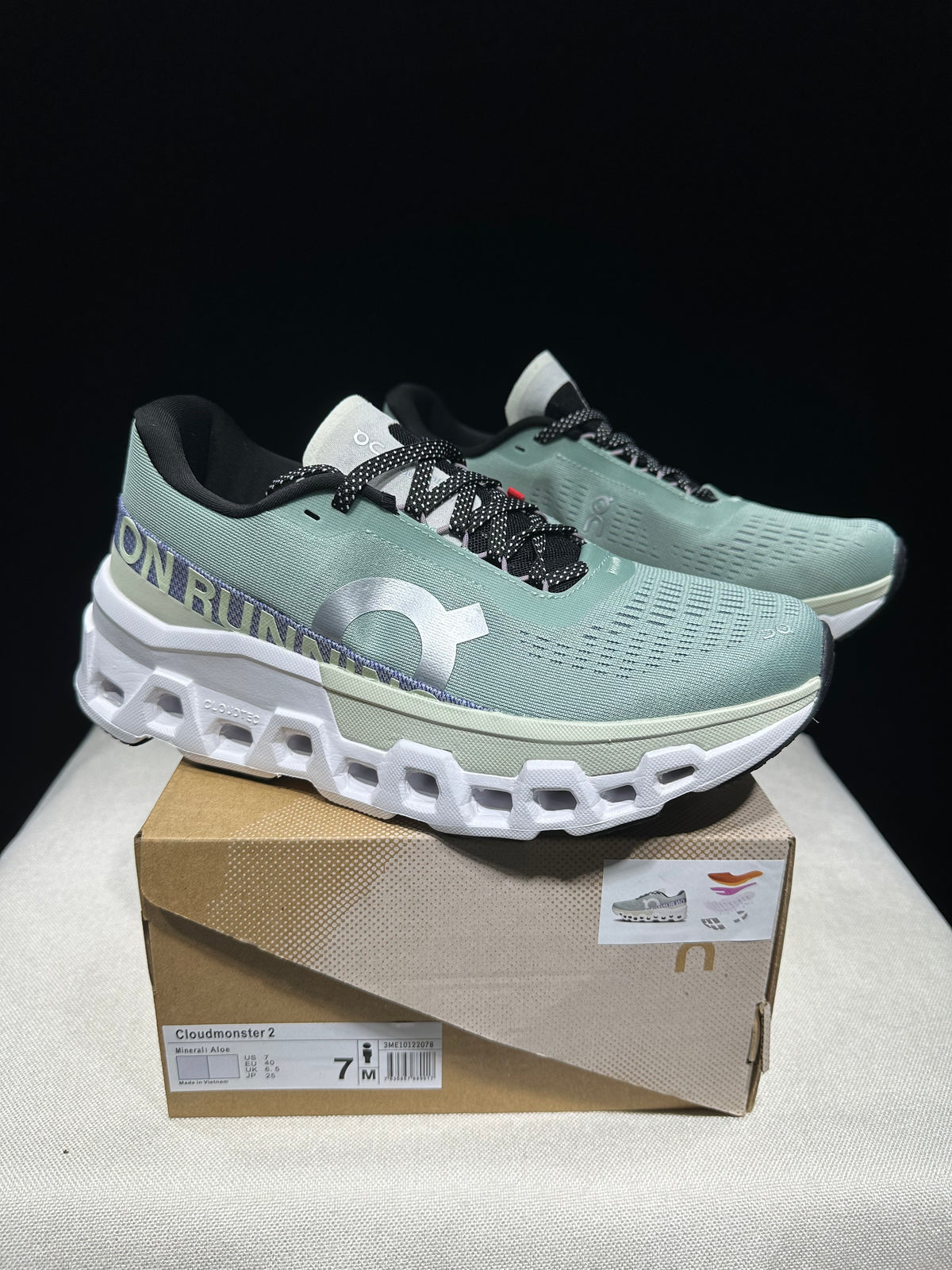 Pair of pale green Cloudmonster 2 shoes displayed on a box with a size label.