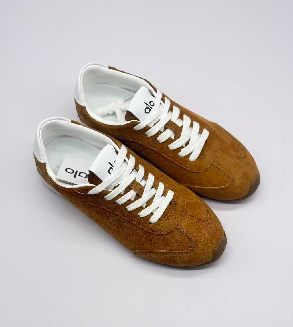 Top three-quarter view of a pair of brown Alo sneakers with white laces and tongue branding.