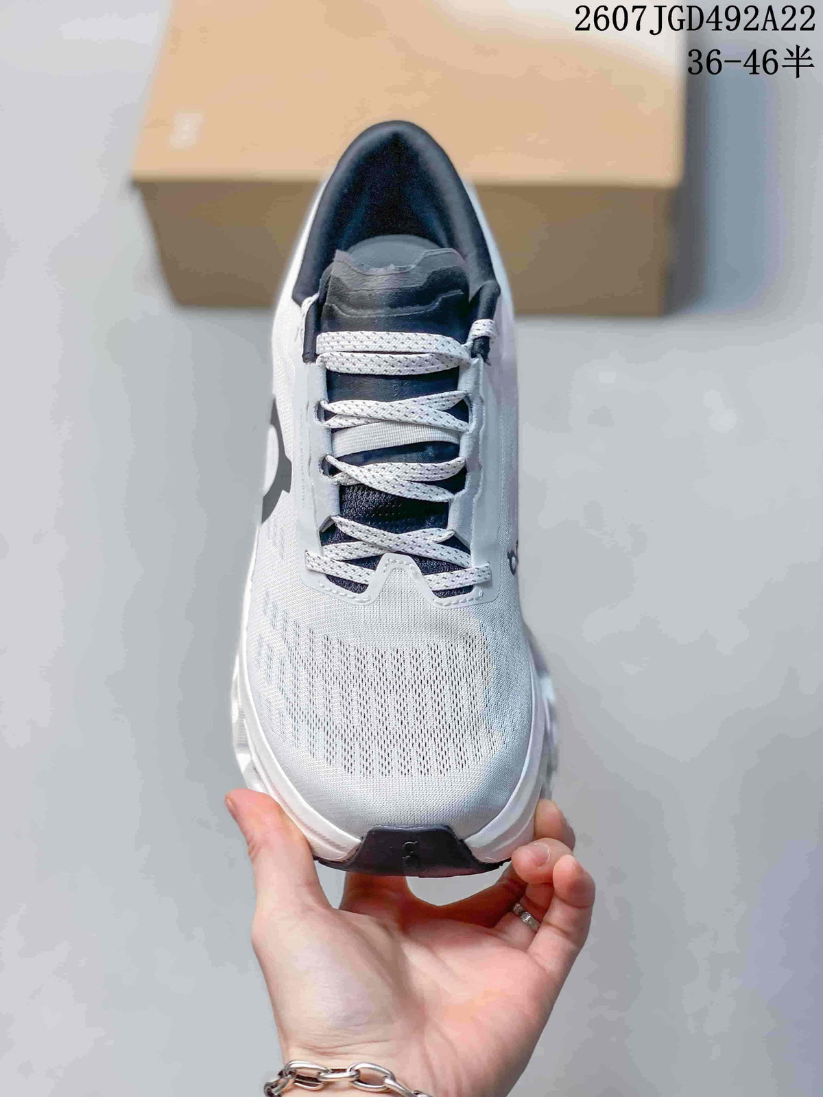 Top view of the white and gray lace-up shoe showing the dark tongue, white laces, and textured toe area; the image displays style code 2607JGD492A22 and size range 36–46.