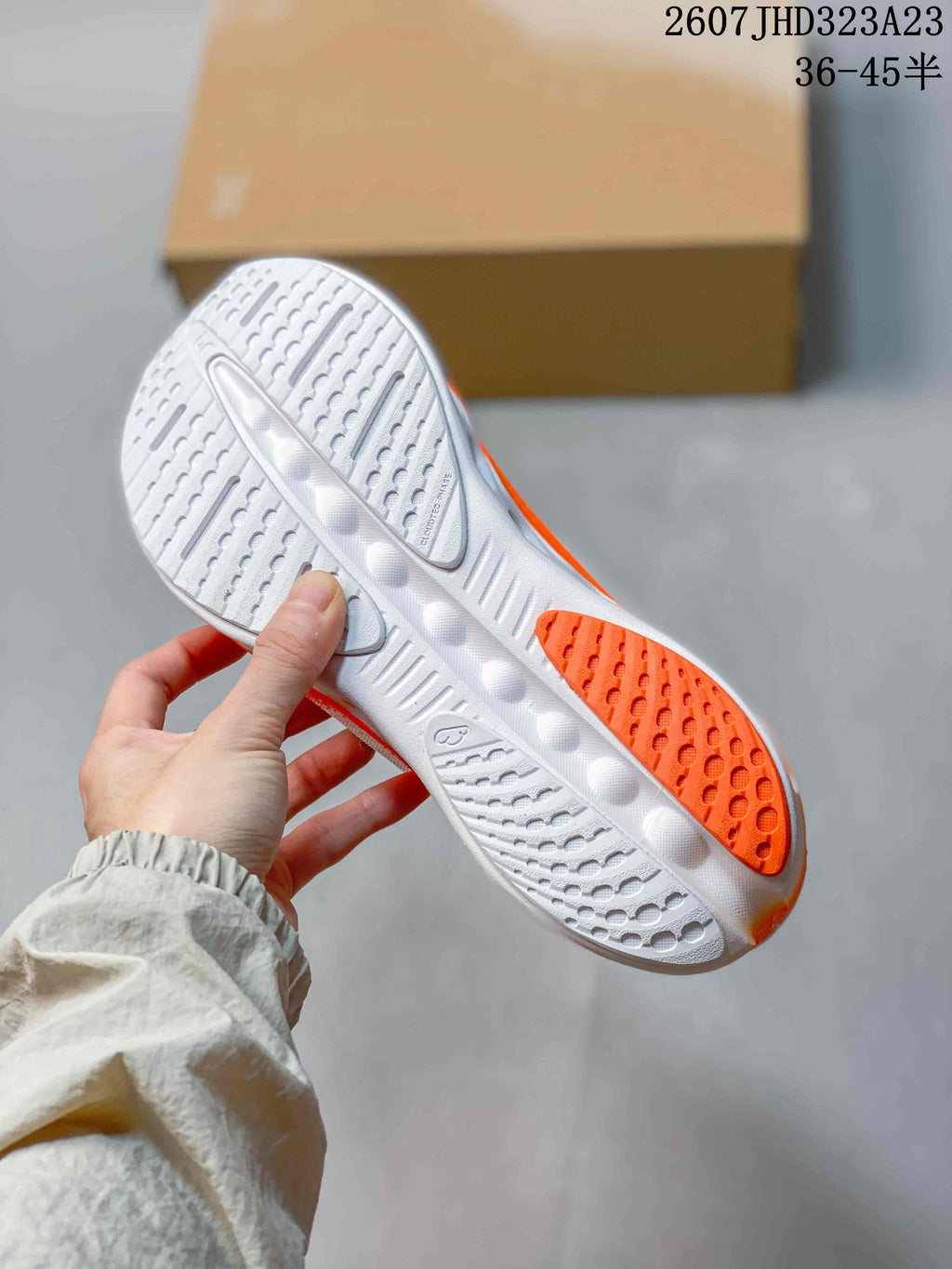 Bottom view of a sneaker showing the white and orange outsole with textured tread and cutout details.