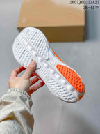 Bottom view of a sneaker showing the white and orange outsole with textured tread and cutout details.