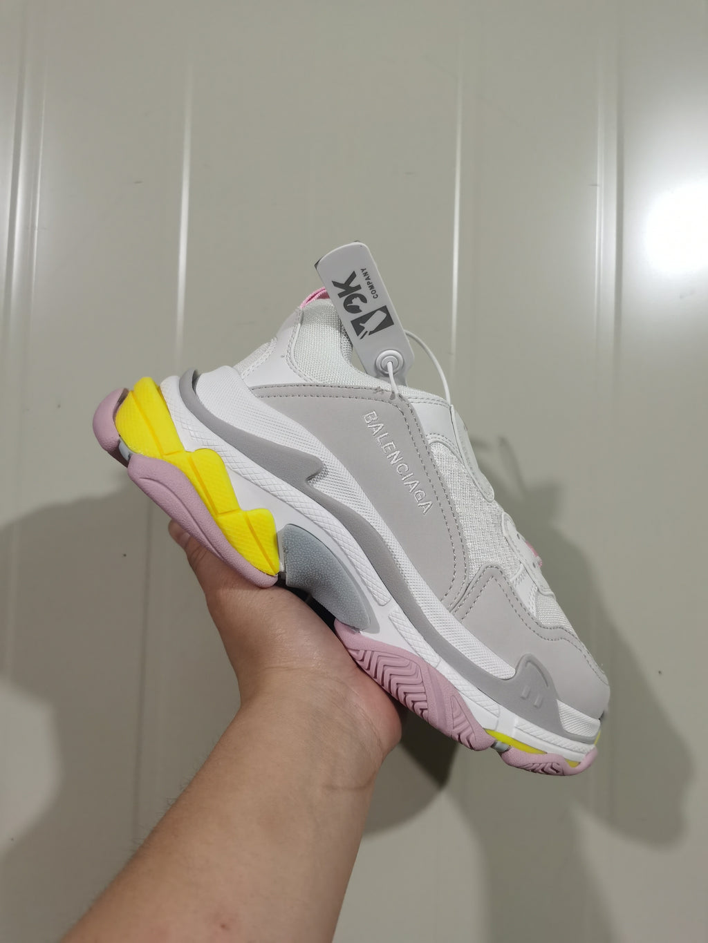 Angled view of the white Balenciaga Triple S sneaker showing layered panels, grey detailing and pink and yellow outsole sections.
