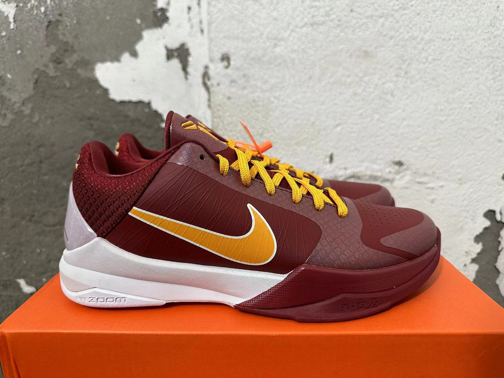 Side view of burgundy Nike Kobe shoe with gold Swoosh, white midsole, and USC-inspired colors