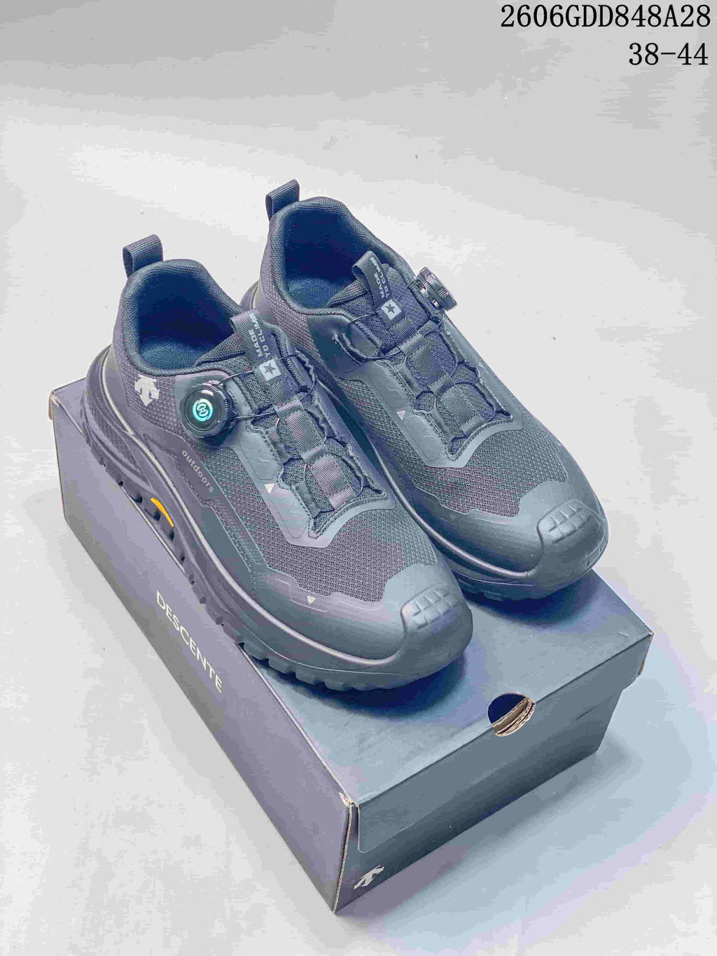 Pair of charcoal DESCENTE outdoor running shoes with dial closures on a branded shoe box; image states sizes 38–44 and style code 2606GDD848A28.