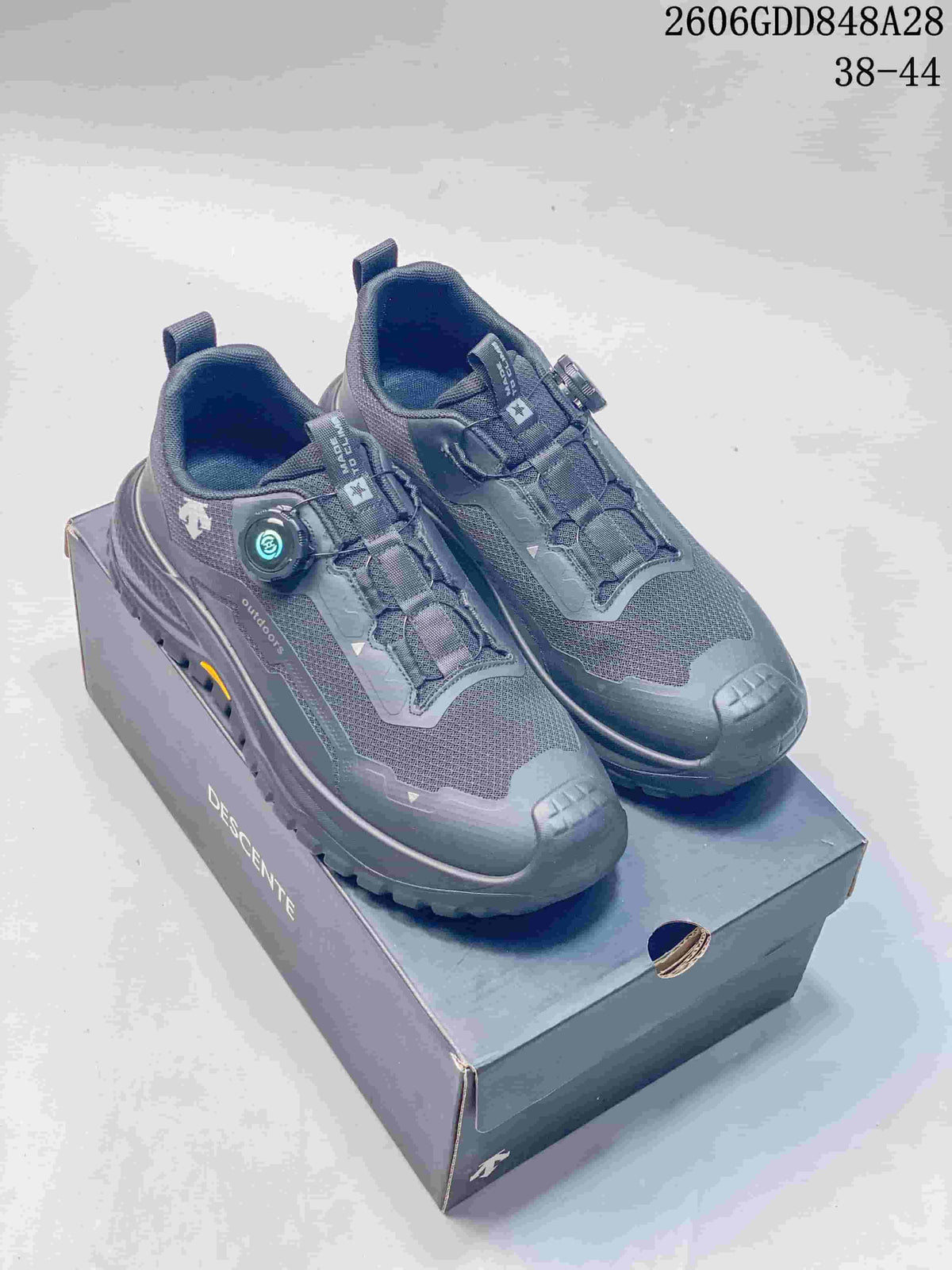 Pair of charcoal DESCENTE outdoor running shoes with dial closures on a branded shoe box; image states sizes 38–44 and style code 2606GDD848A28.