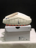 Side view of the light bone Nike Mind 001 mules on the box, with the product label visible.