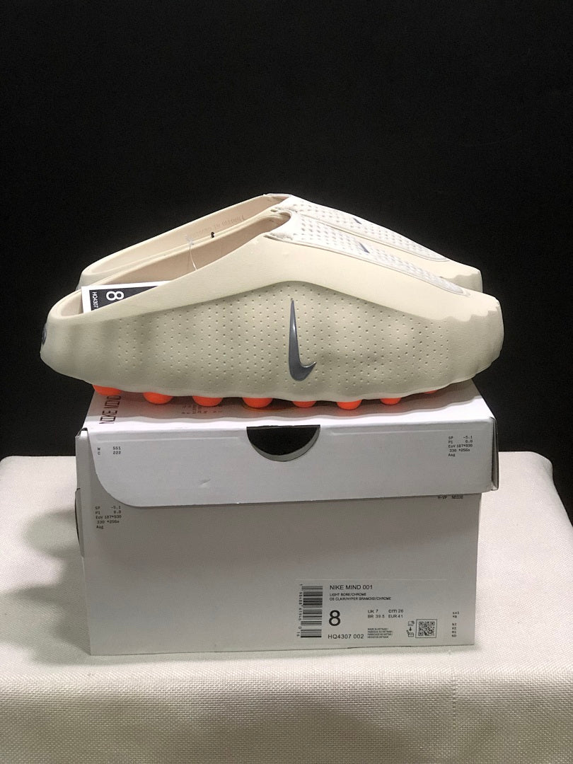 Side view of the light bone Nike Mind 001 mules on the box, with the product label visible.
