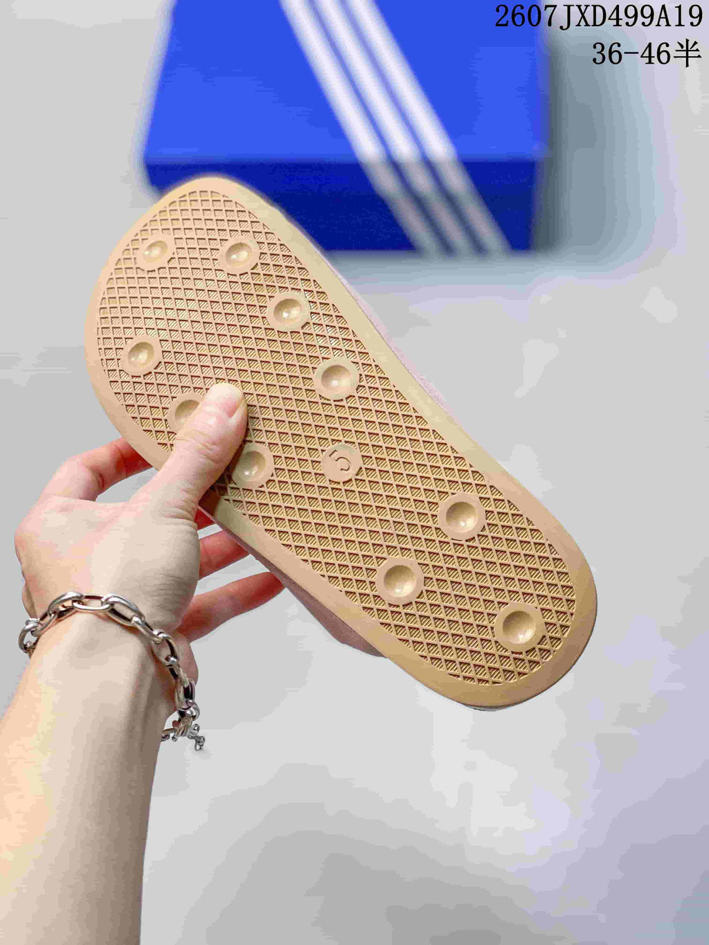 Underside of a pink adidas Adimule mule showing the tan textured outsole and circular tread details; blue adidas-style shoebox in the background.