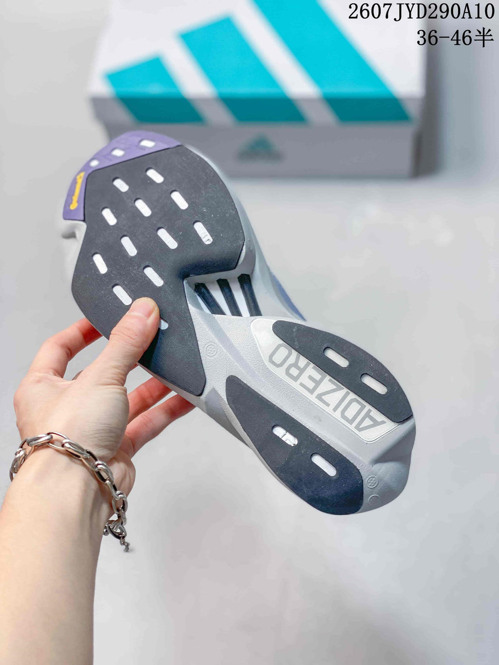 Underside view of the adidas shoe showing a segmented black, gray and purple outsole with elongated traction openings.