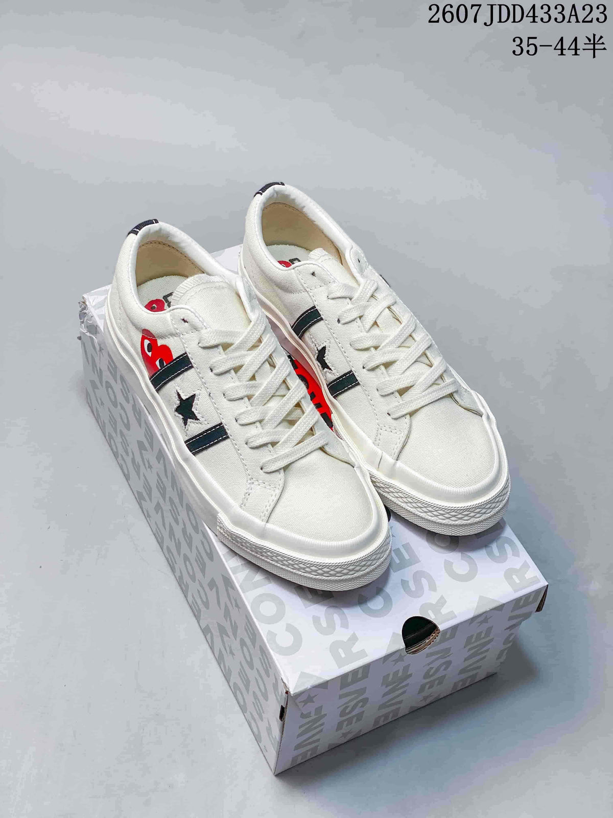 Pair of white low-top sneakers with dark contrast stripes, star emblems and heart-eye graphics displayed on a box.