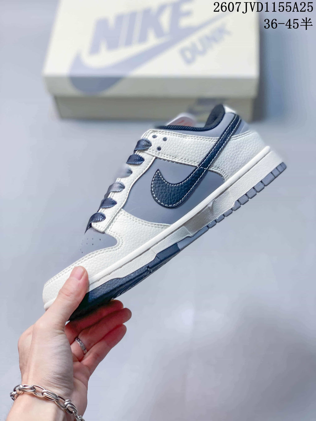 Side profile of the sneaker showing grey and white panels, a dark navy Swoosh and a layered rubber sole.