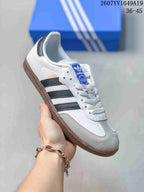 Close side view of a white Adidas Samba sneaker with dark three stripes and a gum-colored outsole.