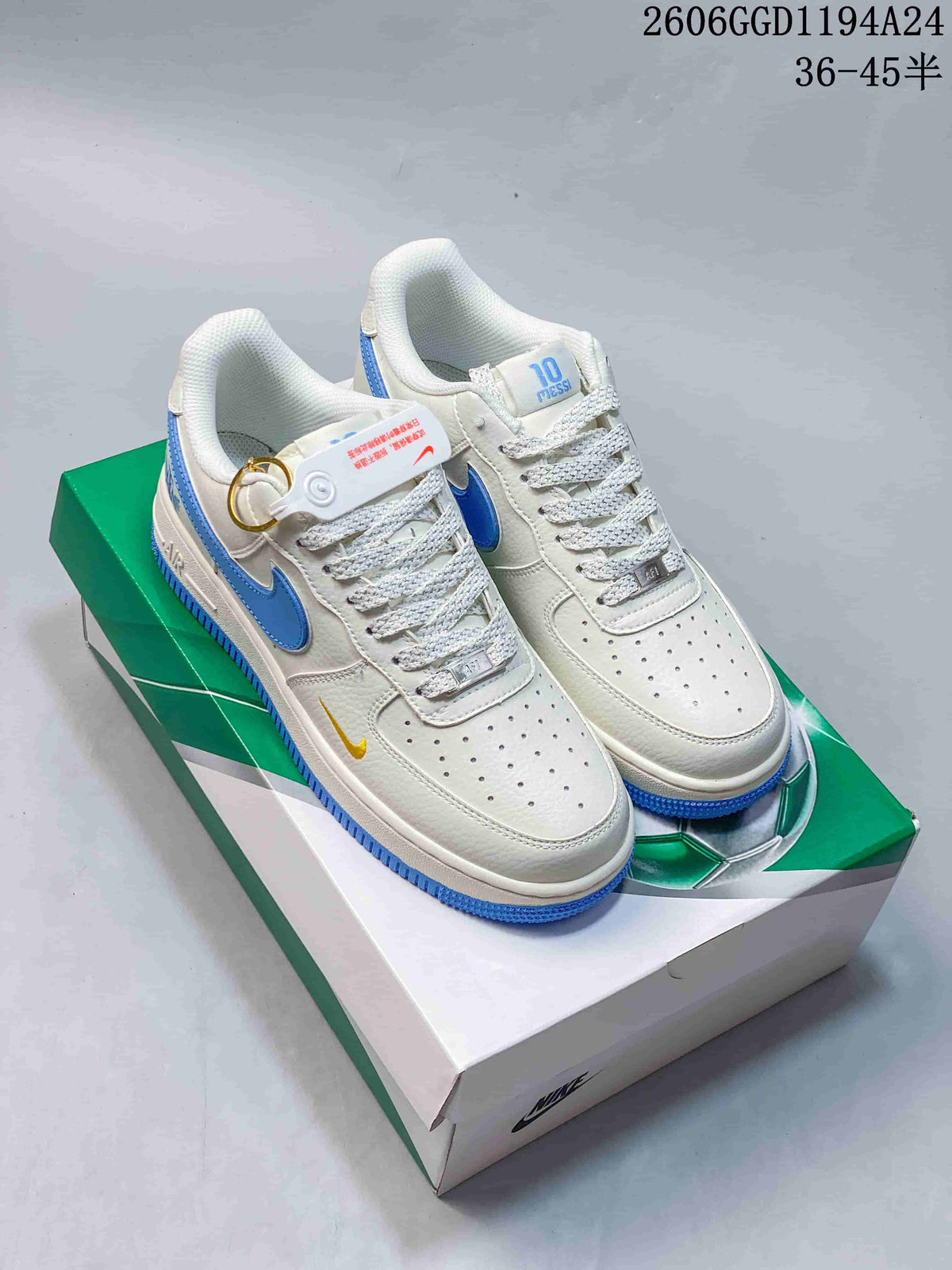 Pair of white and blue Nike Air Force 1-style sneakers with a small metal pendant, shown on a green football-themed box.