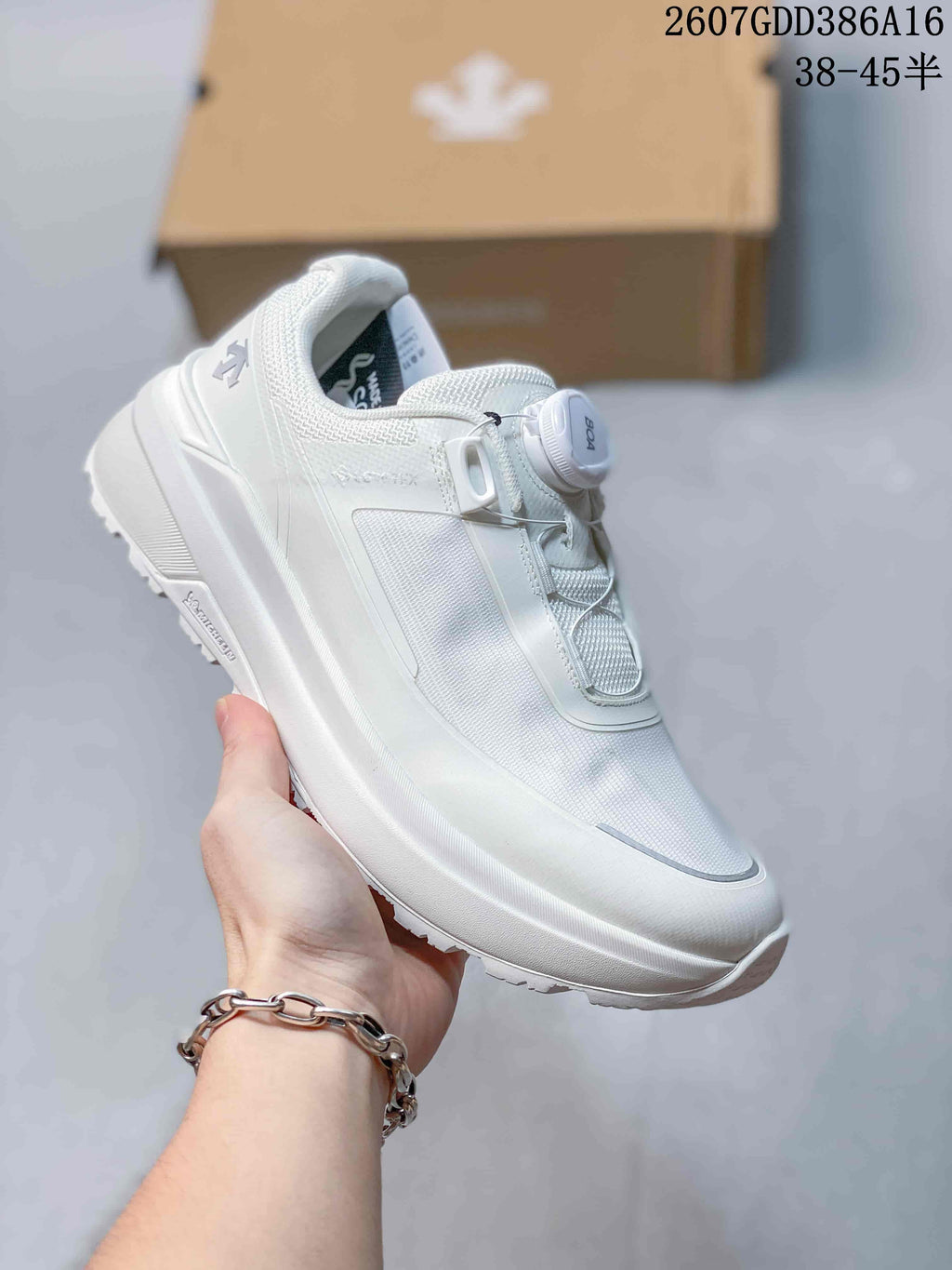 Angled side view of a white DESCENTE sneaker showing the textured upper, BOA dial, layered sole, and visible model detailing.