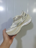 Side view of beige and eggshell Balenciaga sneakers showing layered panels, mesh sections, gray laces, and a sculpted sole.