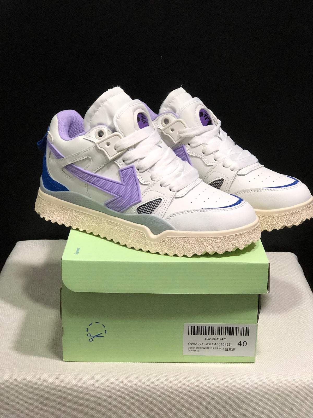 Pair of white Off-White sneakers with purple and blue accents displayed on a green shoe box; the box label shows size 40.