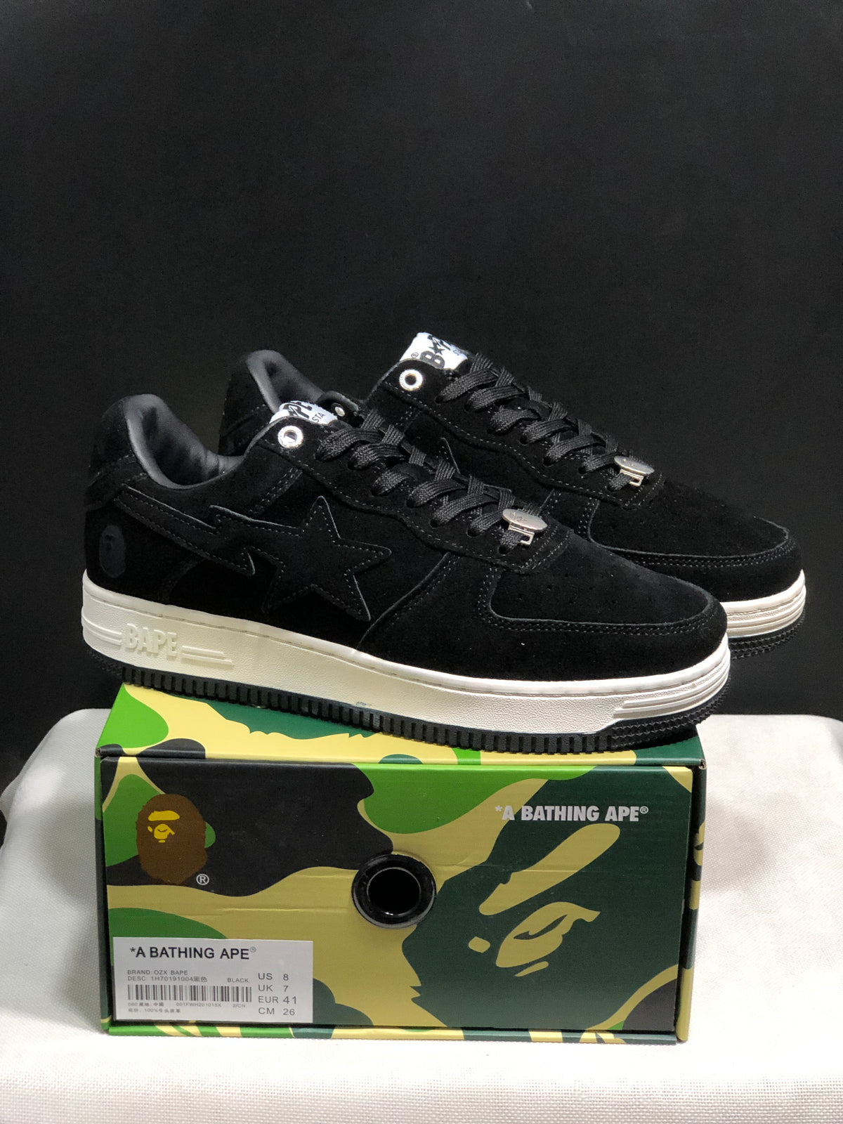 Pair of black BAPE STA low-top sneakers displayed on a camouflage presentation box; the box label shows US 8, UK 7, EU 41 and CM 26.