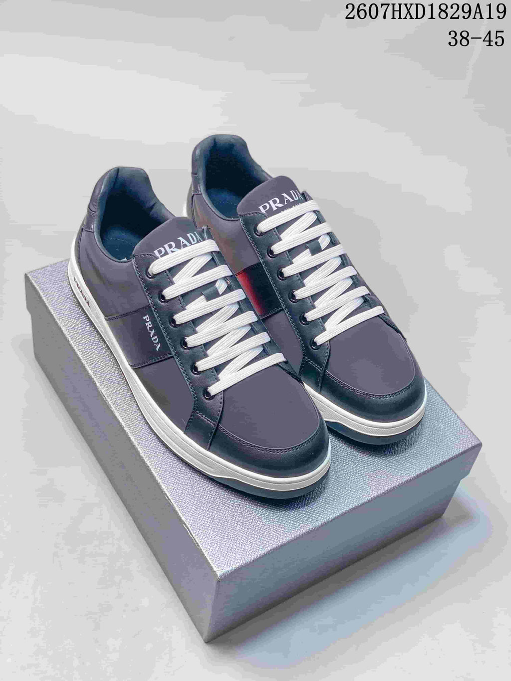 Navy Prada Downtown low-top sneakers with white laces and contrasting light-colored soles on a box; style code 2607HXD1829A19 and size range 38–45 are visible.