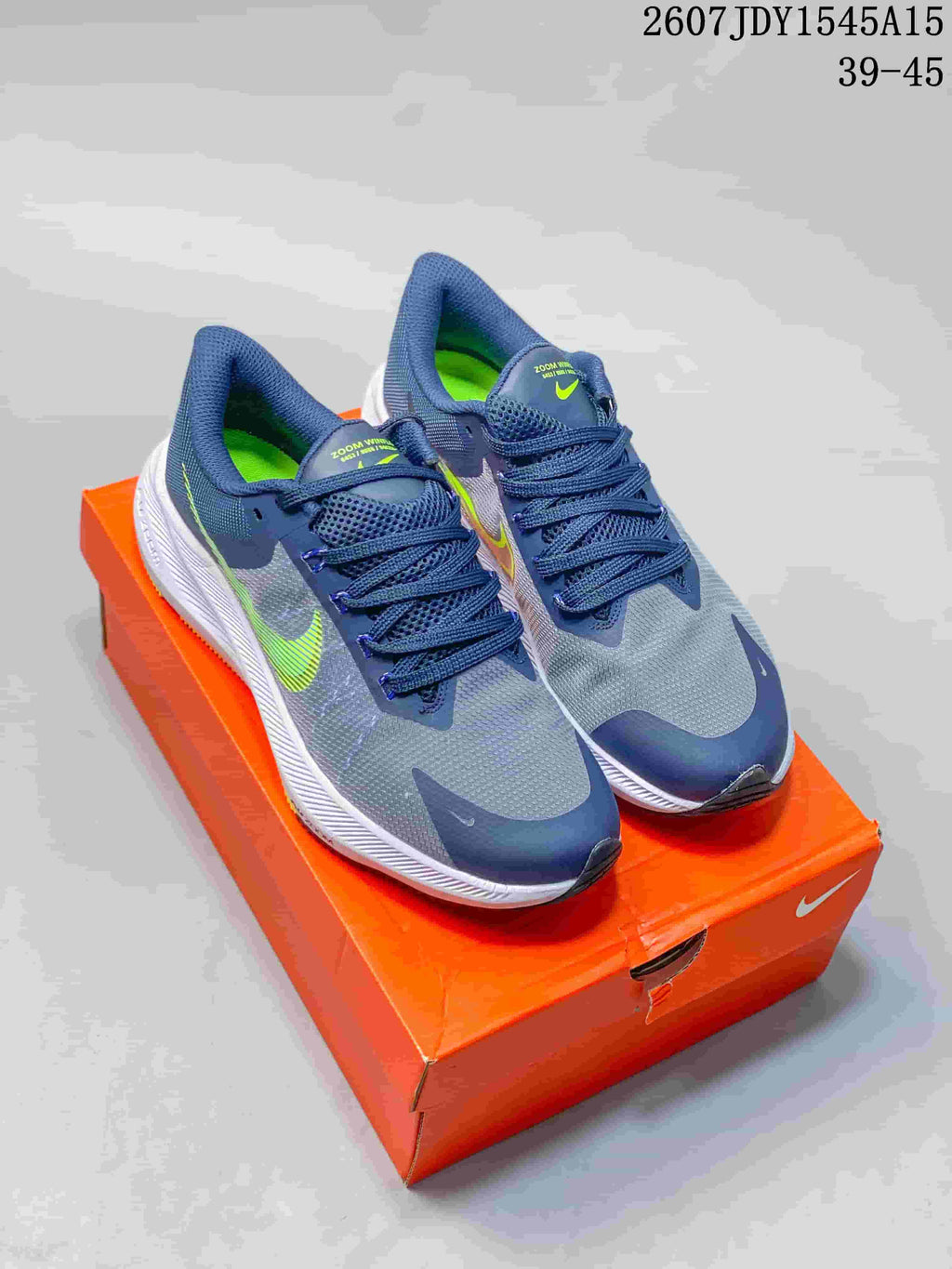 Pair of gray and navy Nike Zoom Winflo 8 running shoes displayed on an orange shoebox, with lime green accents and a visible size range label.