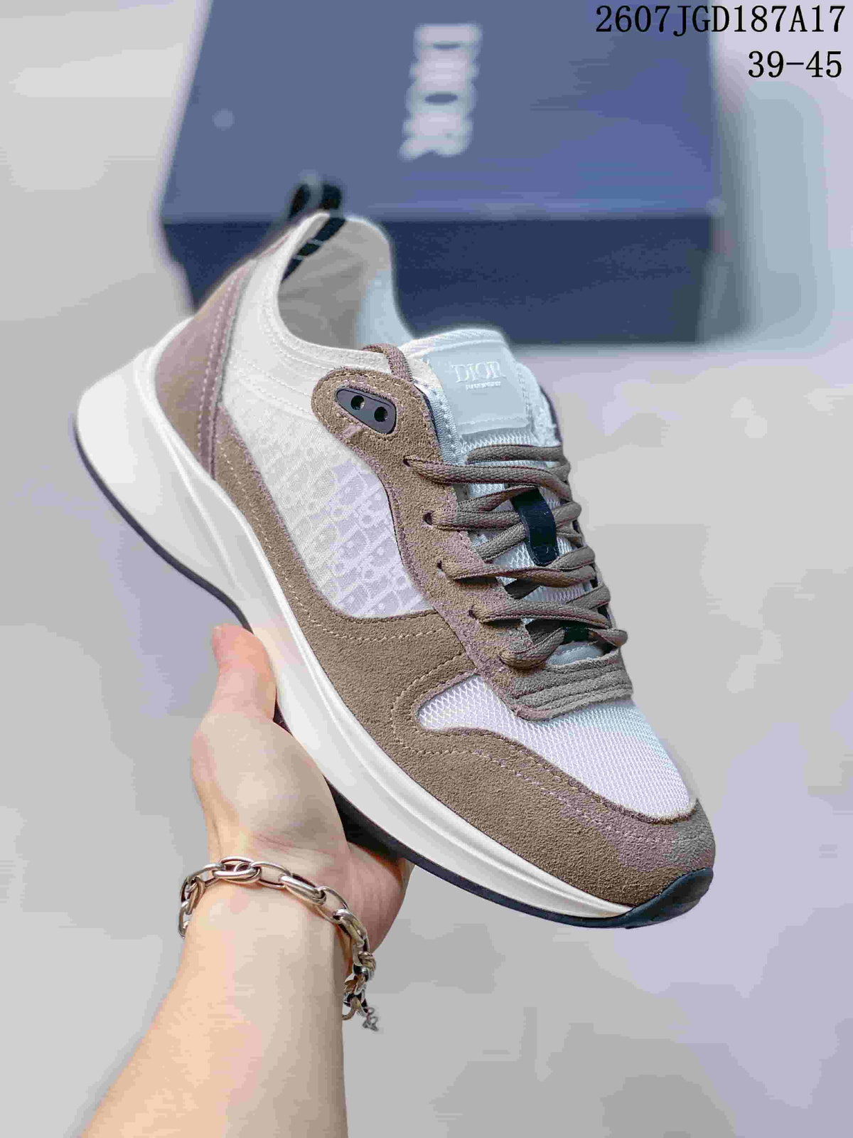 Three-quarter view of a Dior B25 Runner sneaker showing the white and taupe upper, patterned side panel, lace-up front, and layered sole.