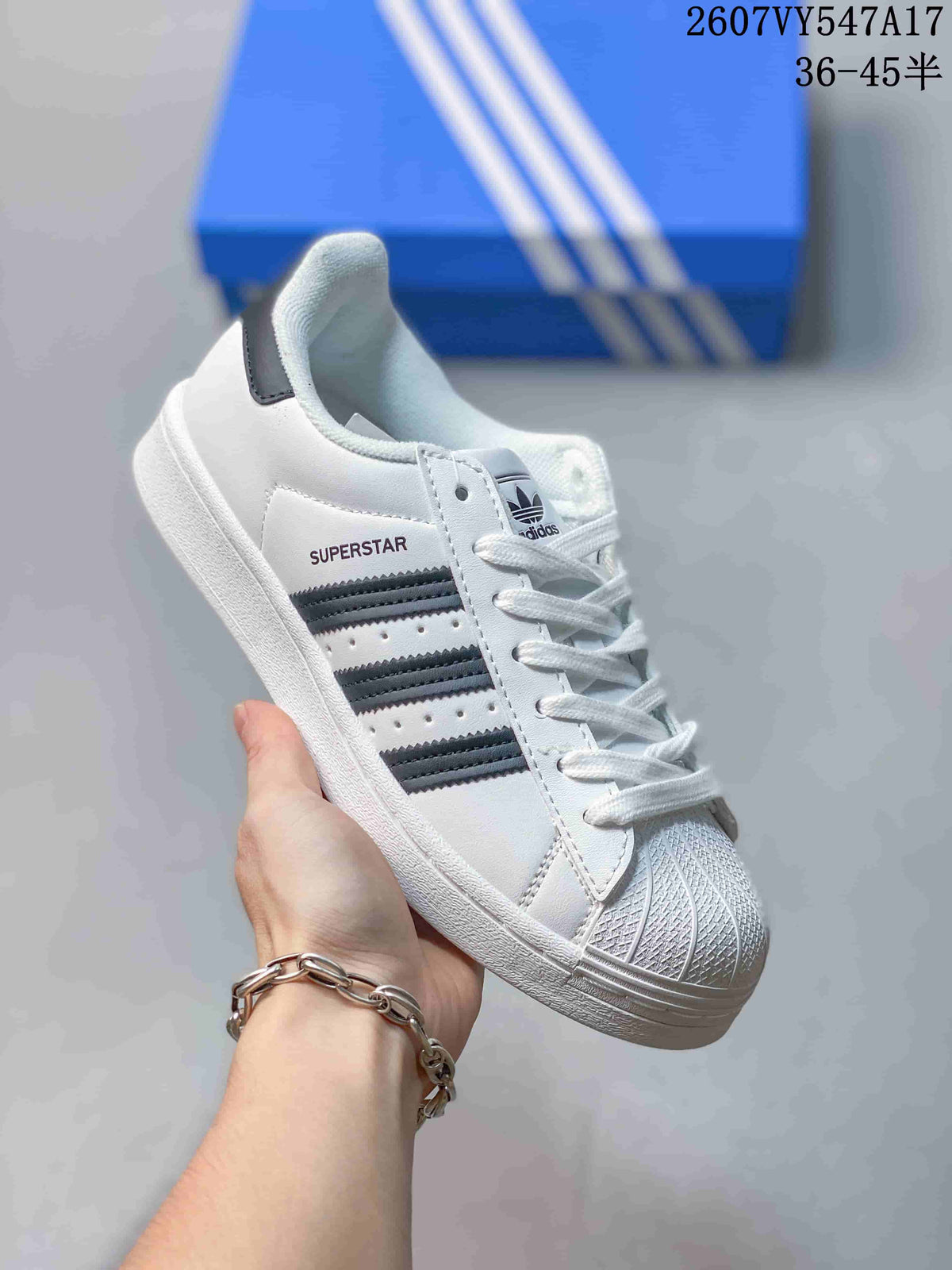 Close-up of a white Superstar sneaker showing the textured shell-style toe, laces, dark side stripes, and Superstar text.