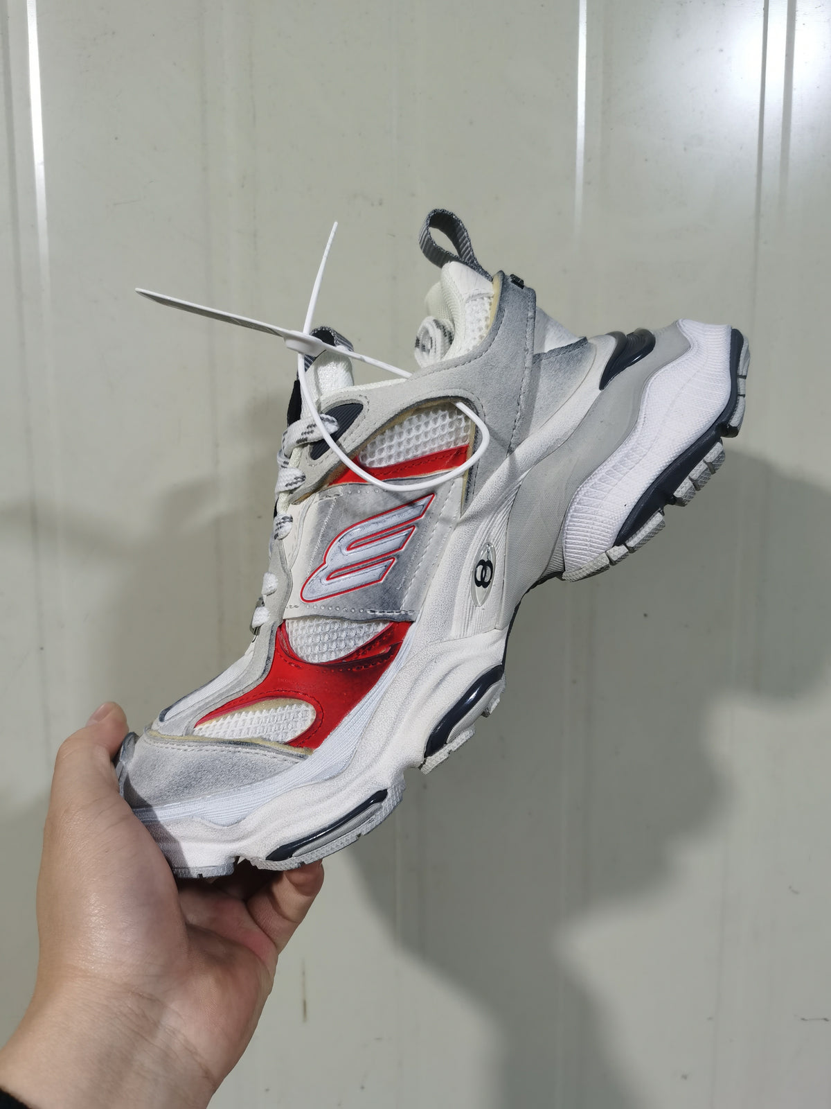 Top and side view of the white, grey and red sneaker showing its lace-up upper, layered construction and contrasting outsole.