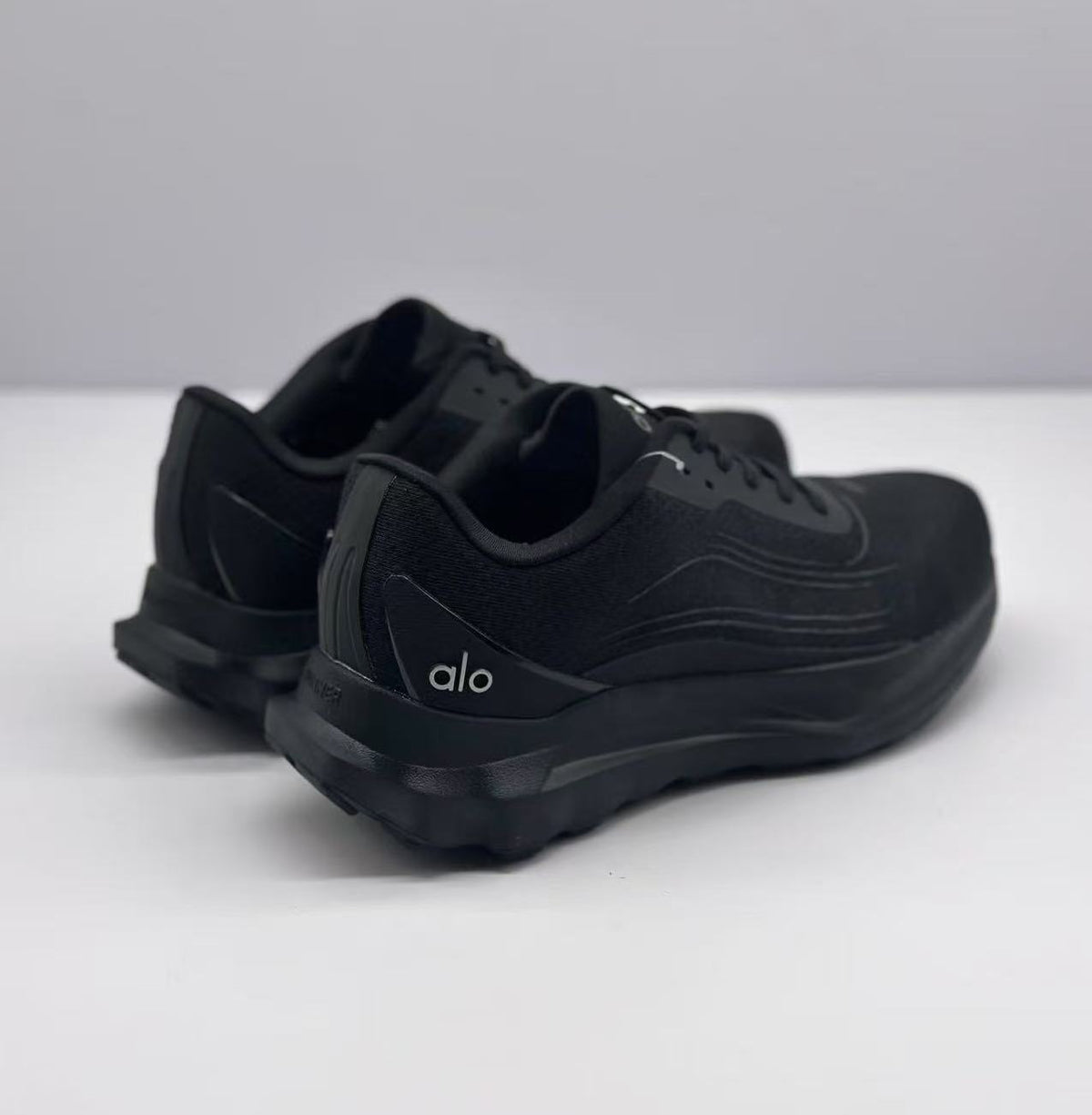 Rear three-quarter view of the black Alo sneakers showing the heel branding, padded collars, and raised outsole.