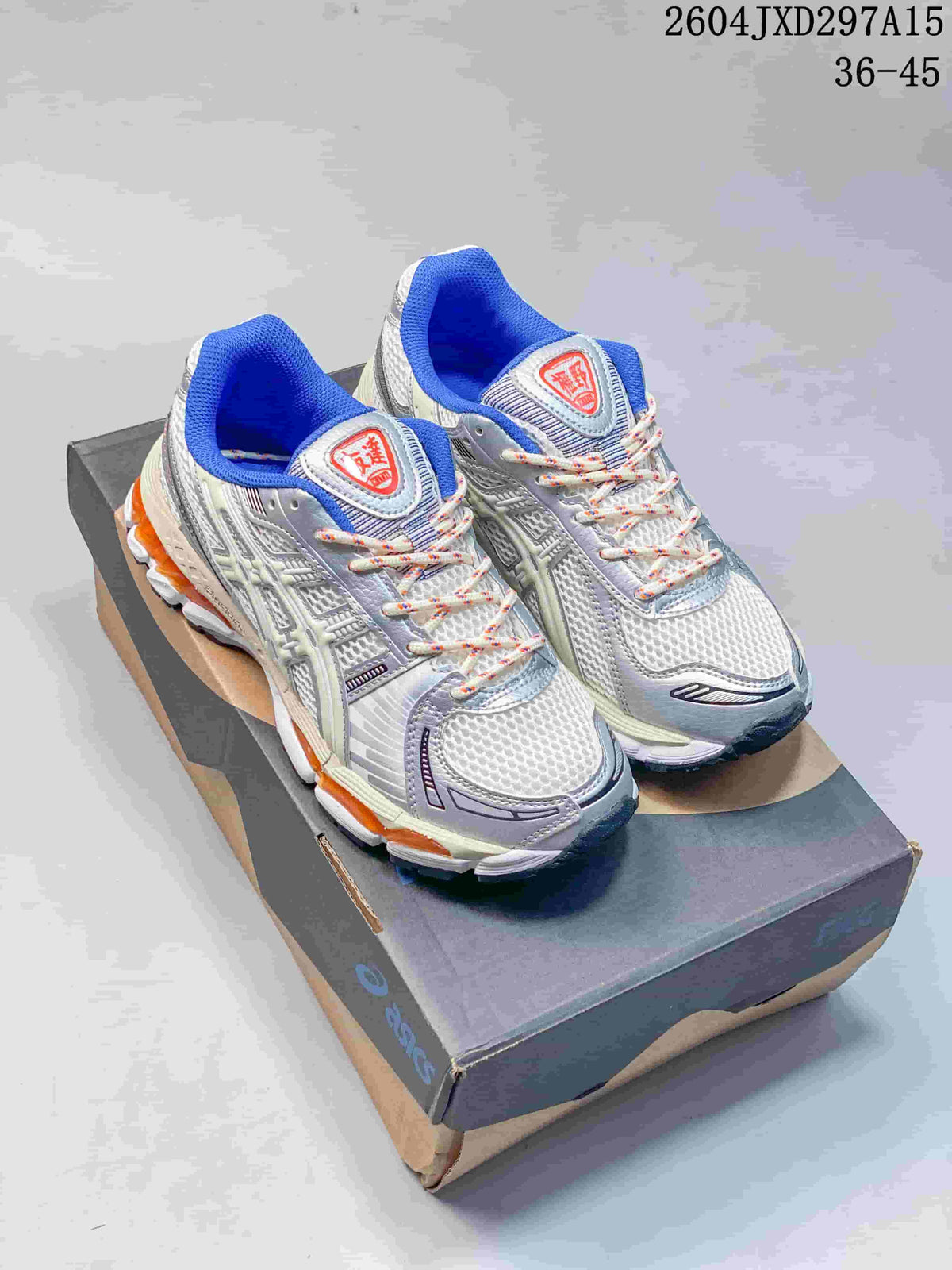 Pair of light grey and off-white ASICS Gel-Kayano 12.1 sneakers with blue lining and orange sole accents, displayed on a shoebox