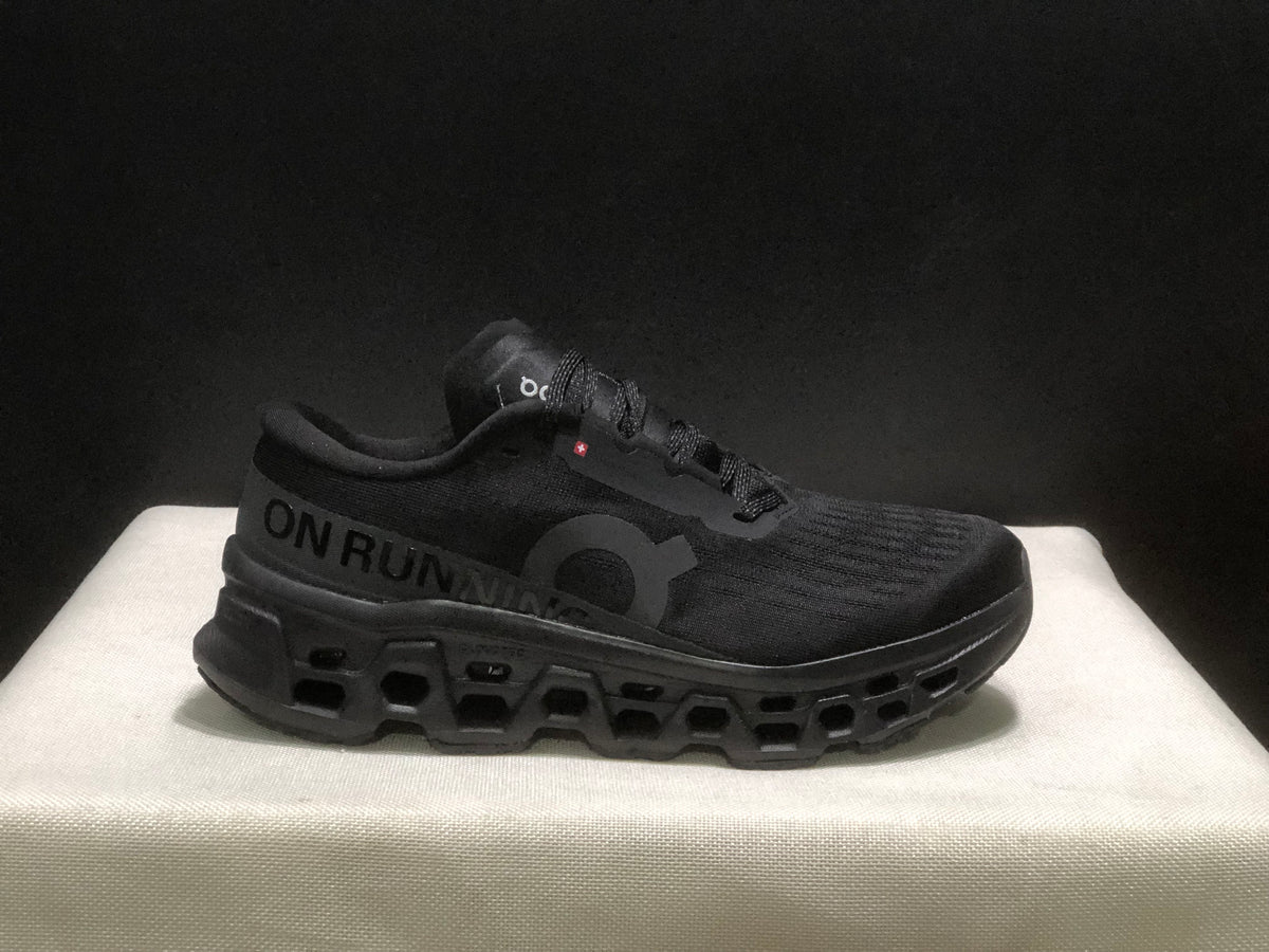 Side profile of a black On Cloudmonster 3 sneaker with visible side branding and segmented outsole.