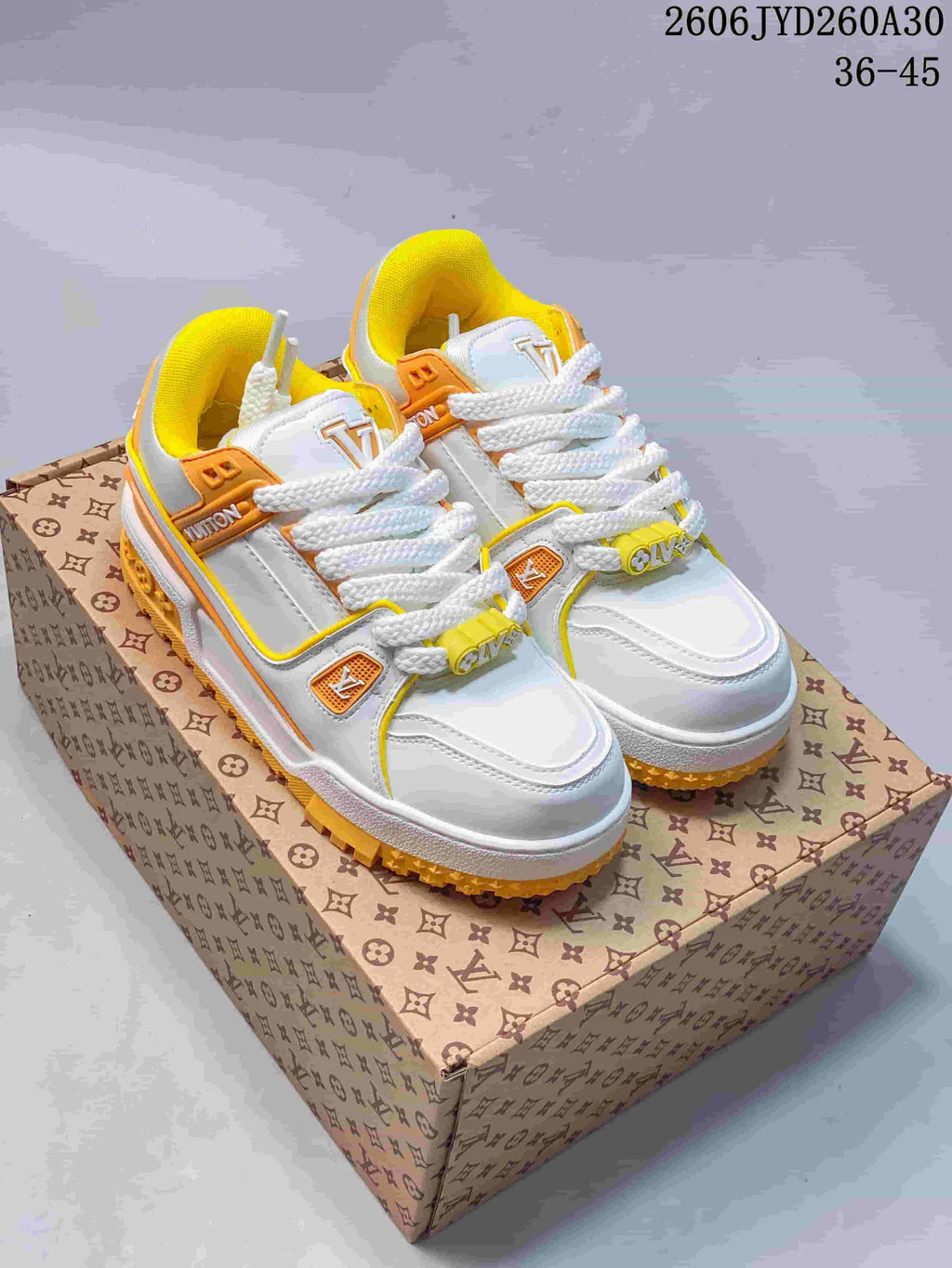 Pair of white Louis Vuitton Trainer Maxi low-top sneakers with orange and yellow accents, shown on a patterned box.