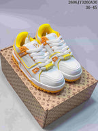 Pair of white Louis Vuitton Trainer Maxi low-top sneakers with orange and yellow accents, shown on a patterned box.