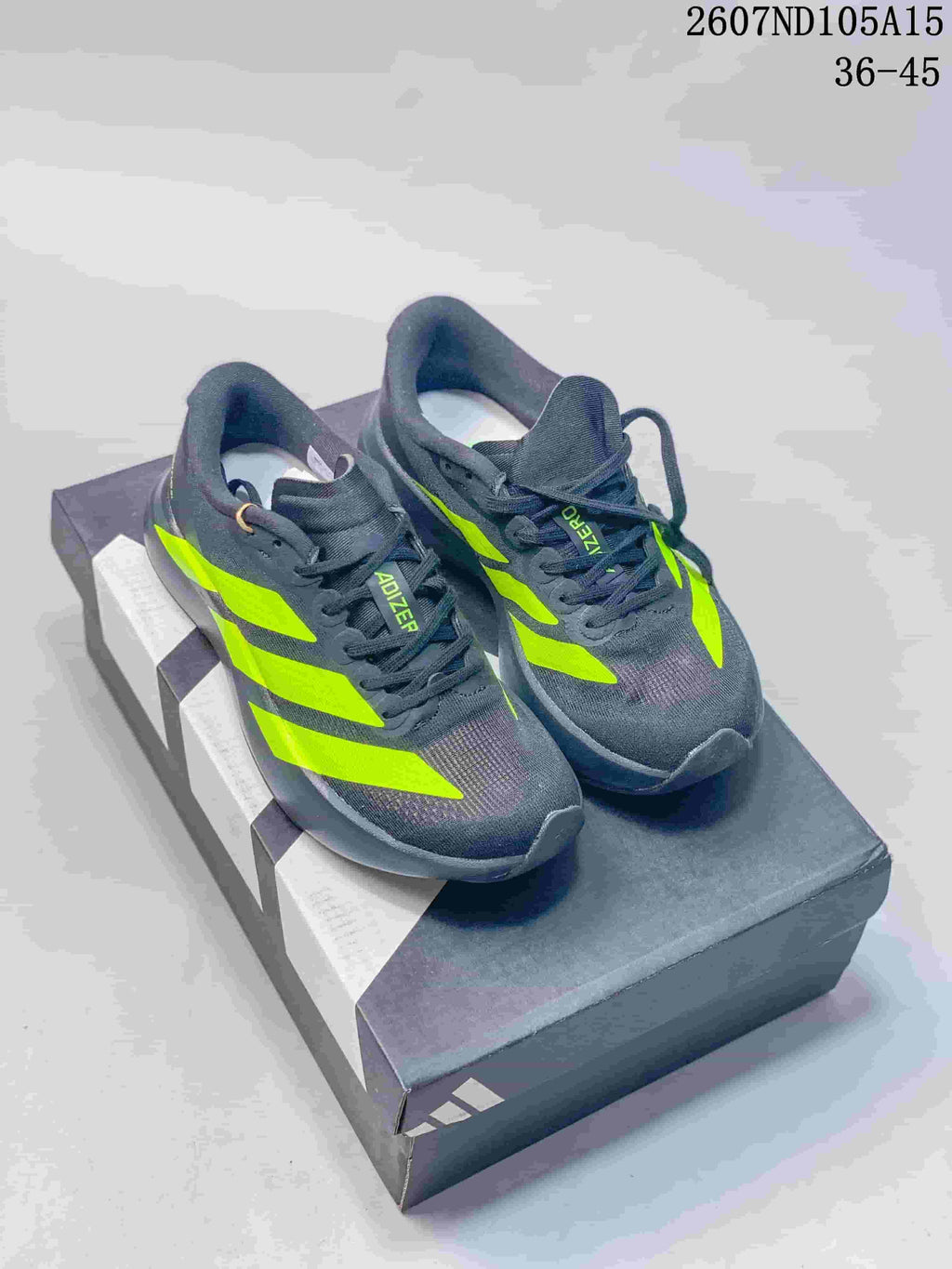 Dark gray Adidas Adizero sneakers with bright green contrast stripes displayed on a shoebox.