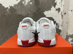 Rear view of white Nike basketball shoes with red heel accents and dark outsole details.