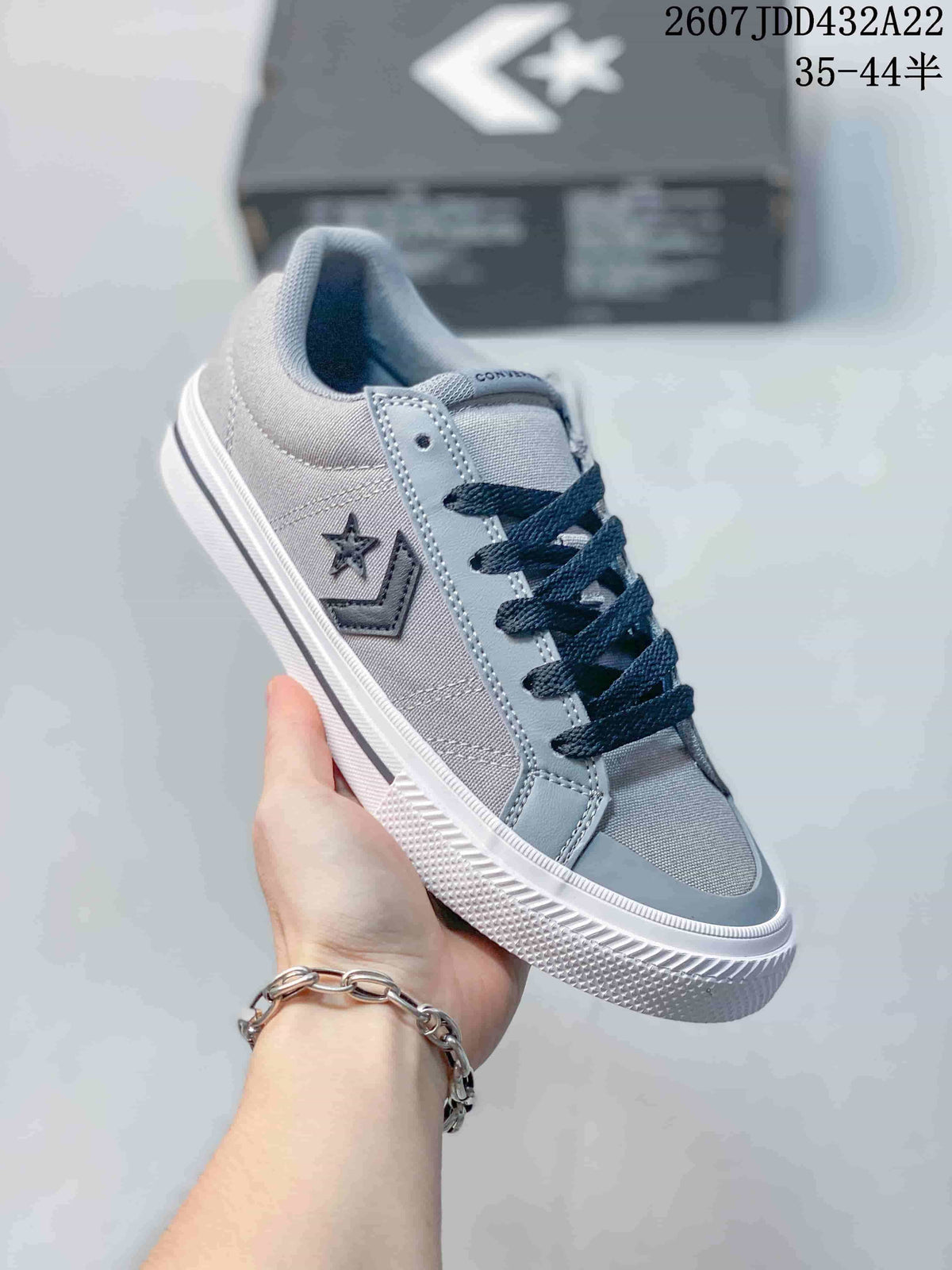 Angled side view of a grey Converse low-top sneaker showing the star-and-chevron side graphic, dark laces, stitched panels, and white textured sole.