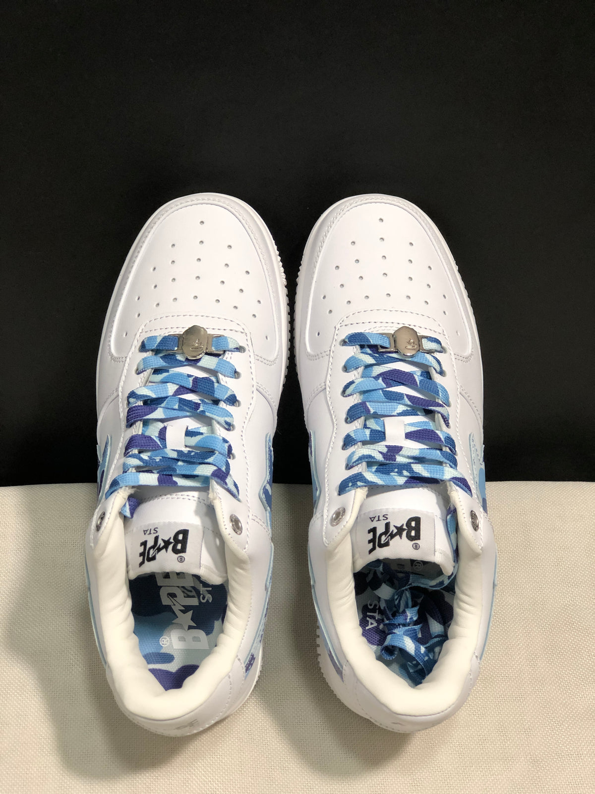 Top-down view showing the white perforated toe boxes, blue patterned laces, and padded collars.