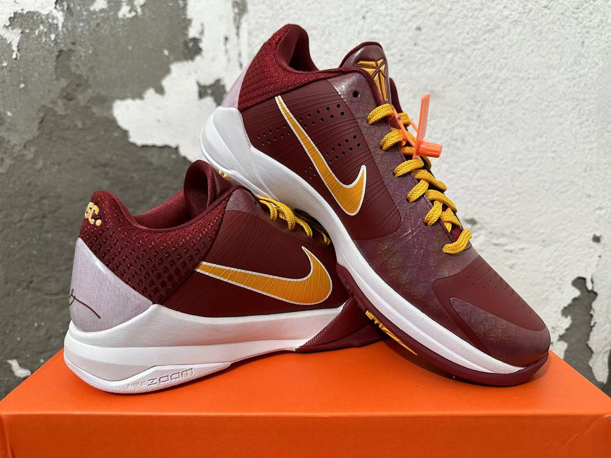 Pair of burgundy Nike Kobe basketball shoes shown from the side with gold Swooshes