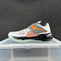 Side view of a white and gray Nike basketball sneaker with orange accents, a midfoot strap, black speckled midsole section, and translucent-looking outsole.